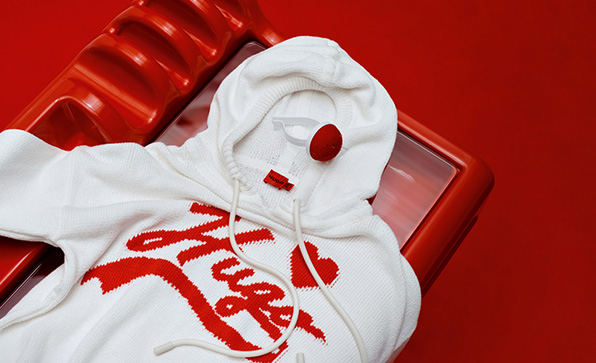 A white knit hoodie with a red cursive HUGO logo on a red background (Photo)