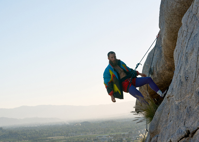 Powerful Circles – Person climbing up a boulder putting on a BOSS x PHIPPS padded jacket (Photo)